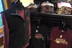 A mannequin wearing a vest and shirt, with other shirts on display.