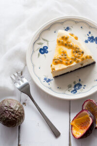A slice of passionfruit cheesecake on a plate with a fork and passionfruit.