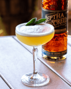 cocktail, likely a sour, garnished with two sage leaves.