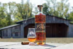 Photo of Jeptha Creed bourbon bottle and glass with bourbon accompanied by a cigar.
