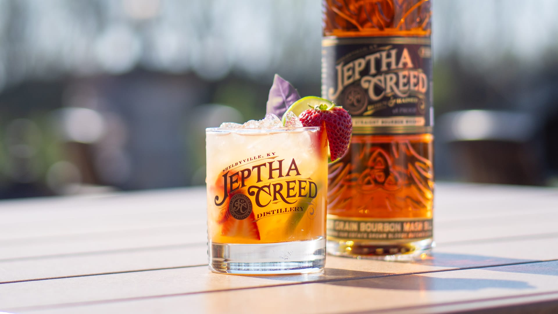 Photo of a Jeptha Creed cocktail and bottle of bourbon on table outside.